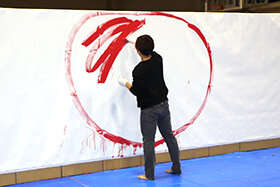 写真：大きな紙に大きな赤丸を描き、中を赤くぬる学生。