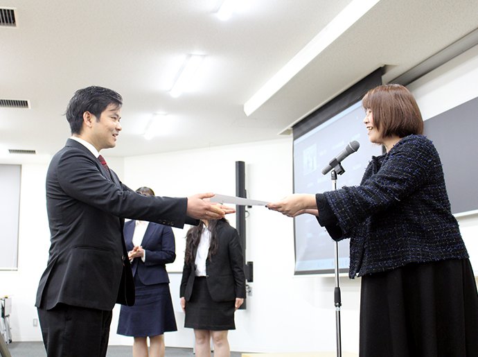 写真：プレゼン画面とともに4人で並ぶ発表者たち