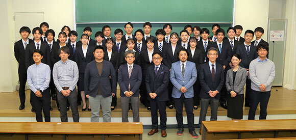 写真：スーツ姿の学生と教員の集合写真