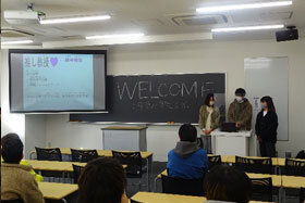 写真：「WELCOME」と書かれた黒板の前で話す3人