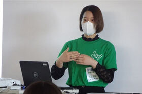写真：緑のユニフォームTシャツを着て発表をする女学生