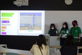 写真：緑のユニフォームTシャツを着てプロジェクターで発表をする学生たち