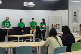 写真：緑のユニフォームTシャツを着て発表をする学生たち