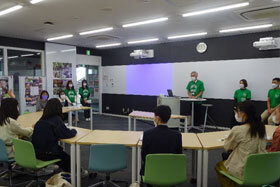 写真：緑のユニフォームTシャツを着て発表をする学生たち
