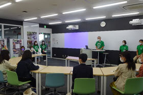 写真:緑のユニフォームTシャツを着て発表をする学生たち